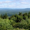 A scenic view of a hilly, forested landscape with light blue skies and a handful of small clouds