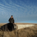 An uniformed adult stands in front of one end of a long drain pipe in a grassy prairie