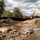 muddy, rocky riverbed with excavator on hill on right