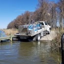 A truck with a large metal tank banks into a boat launch.