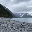 People stand on clean rocky beach with pile of trash bags full of debris they removed.