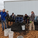 5 youth workers measuring out a brown, soil-like material onto a grate