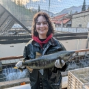 WaterCorps Service Member holding an adult chum salmon. Fish hatchery and skyline in the background.