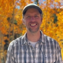 Geoff Bedrosian standing in front of trees with golden leaves
