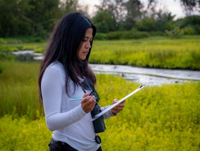 Nikki Imamura, a U.S. Fish and Wildlife Service biologist, stands in a green wetland field. 