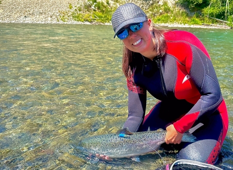Service intern in river holding a Chinook Salmon with a radio tag on it's dorsal fin.