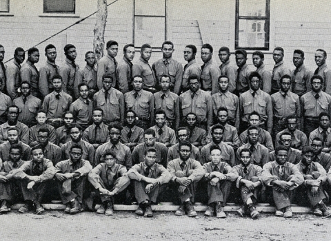 Black and white photo of more than 100 young African American men in uniform posing in front of a building