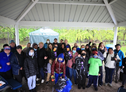 A large group of people standing under a pavilion smiling. A tent is seen in the background with the words "Elizabeth NJ Partnership" printed on the front