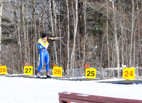 Member of the Massachusetts National Guard Biathlon Team stands in a shooting lane aiming at targets. 