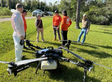 Five people stand in a semi-circle around a drone positioned on the ground