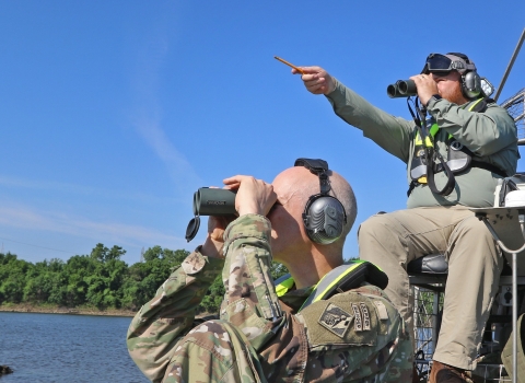 2 men sitting in boat using binoculars, using headphones