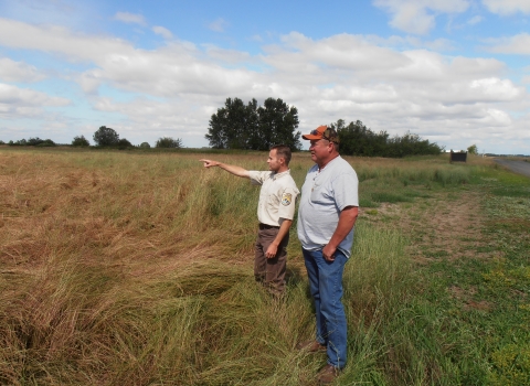 A biologist and a landowner standing in a grassy field looking at the landscape as they discuss restoration potential